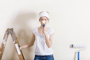 Frau mit Pinsel in der Hand steht auf einer Leiter und freut sich aufs Malen