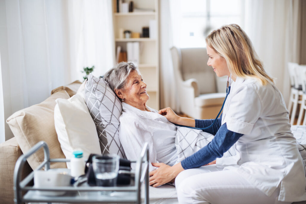 Eine Pflegerin untersucht eine kranke Seniorin, die zu Hause im Bett liegt, mit einem Stethoskop