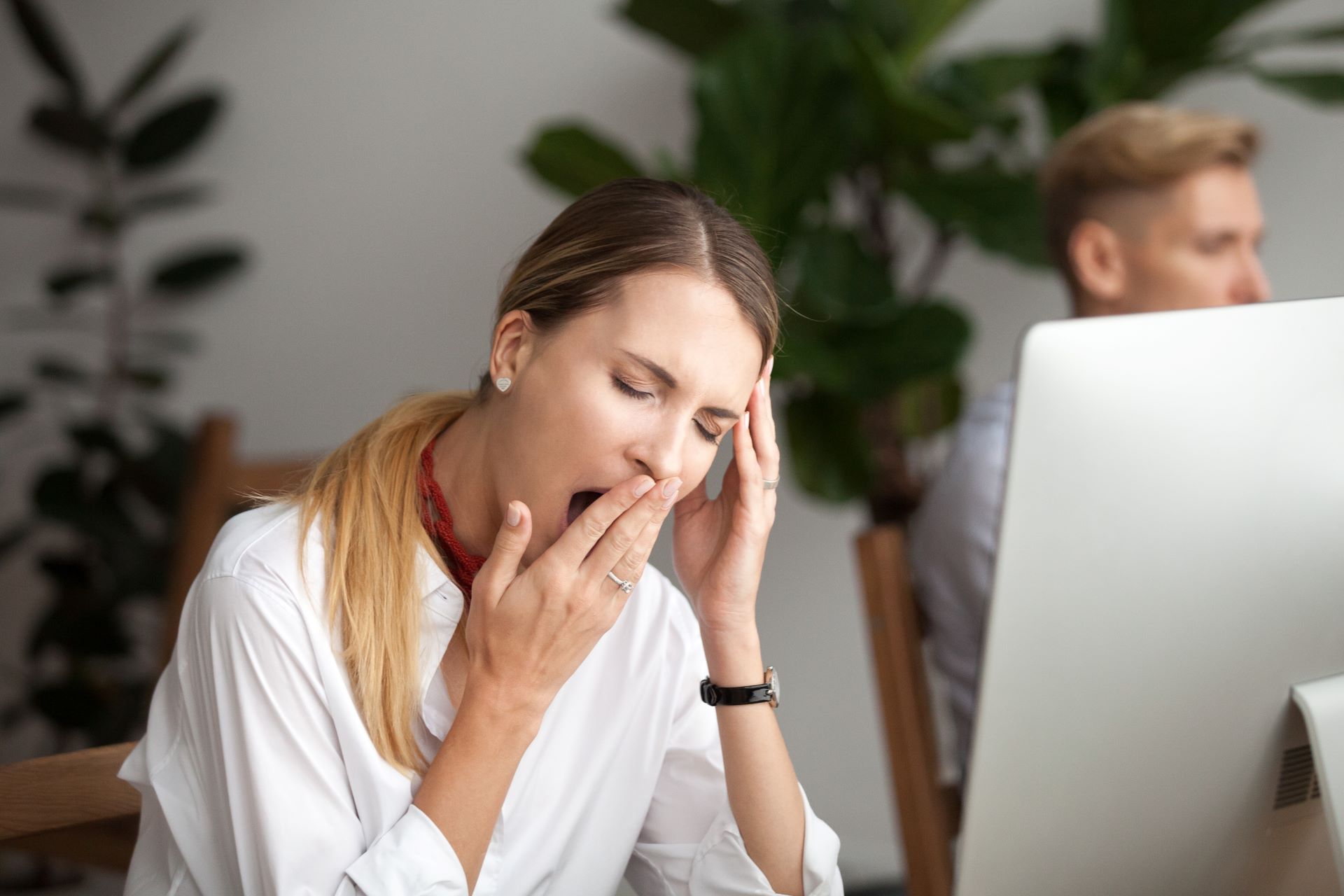 Frau gähnt am Schreibtisch wegen Schlafproblemen durch ADHS.